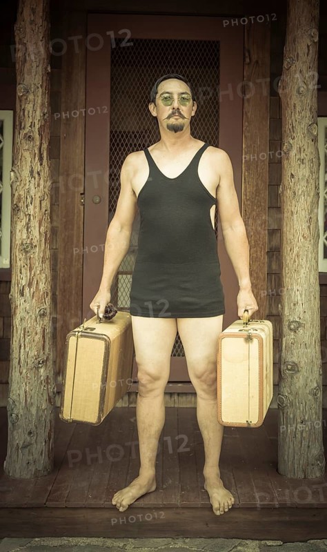 Goofy gentleman dressed in 1920's era swimsuit holding suitcases on porch of cabin