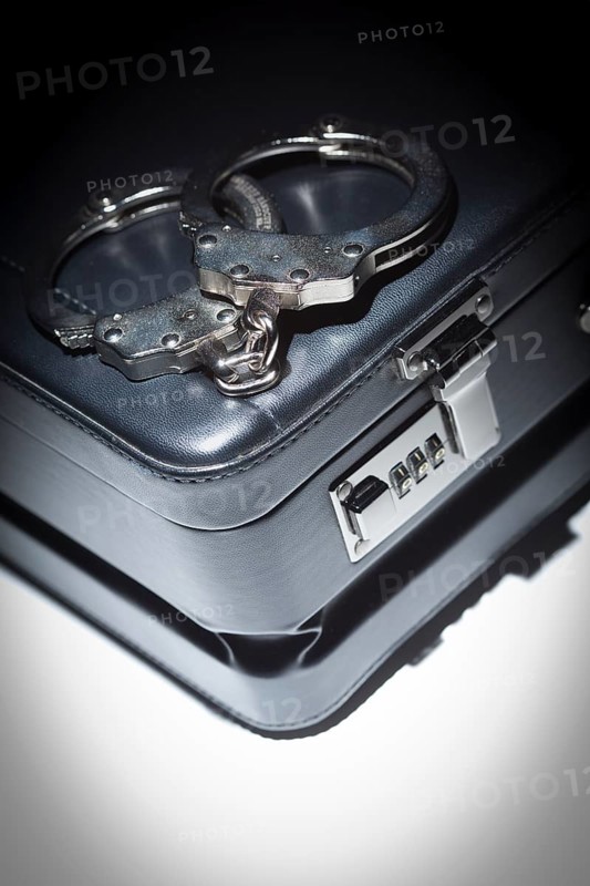 Pair of handcuffs and briefcase under spot light abstract