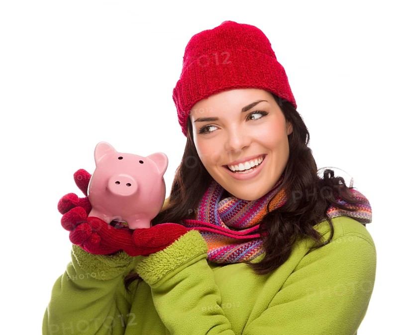 Happy mixed-race woman wearing winter clothing holding piggybank isolated on white background