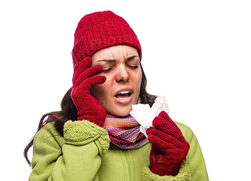 Sick mixed-race woman wearing winter hat and gloves blowing her sore nose with a tissue isolated on white background