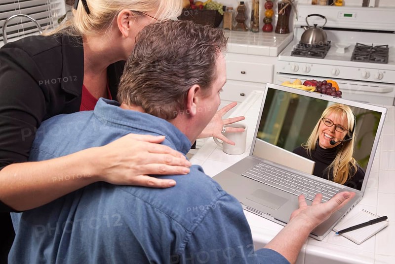 Couple in kitchen using laptop with customer support woman on the screen