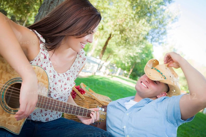 Happy attractive mixed-race couple with guitar and cowboy hat in the park