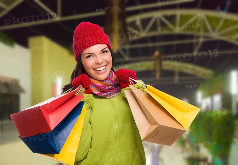Pretty warmly dressed mixed-race woman in outdoor mall with shopping bags