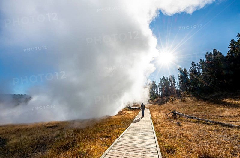 Hiker on footbridge next to steaming hot spring