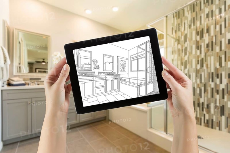 Hands holding computer tablet with master bathroom drawing on screen and photo behind