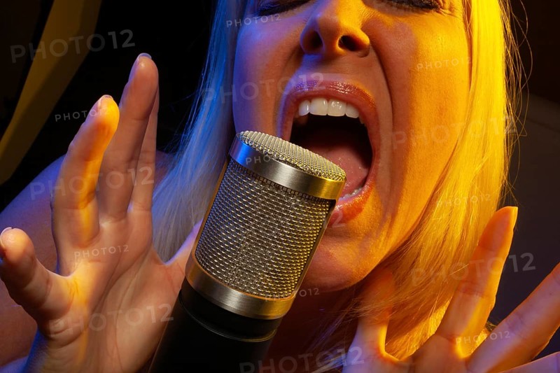 Female vocalist under gelled lighting sings with passion into condenser microphone