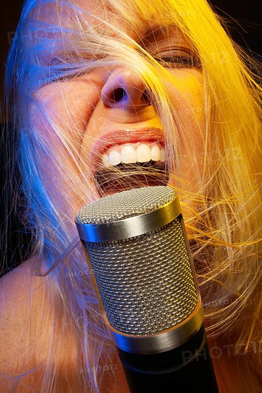 Female vocalist under gelled lighting sings with passion into condenser microphone