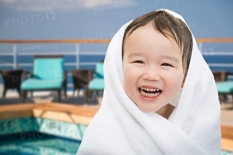 Happy cute mixed-race chinese and caucasian boy on cruise ship wrapped in A towel