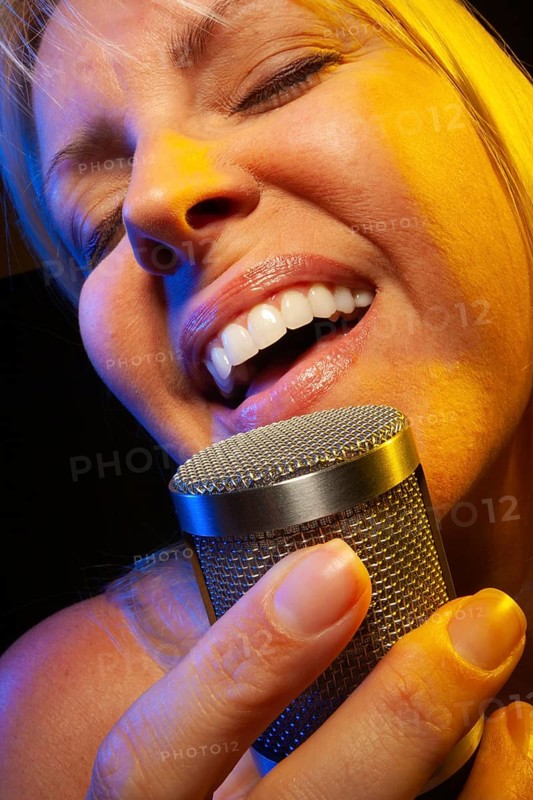 Female vocalist under gelled lighting sings with passion into condenser microphone