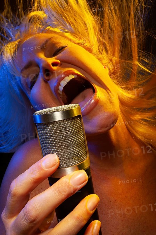 Female vocalist under gelled lighting sings with passion into condenser microphone