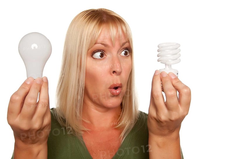 Funny faced woman holds energy saving and regular light bulbs isolated on a white background
