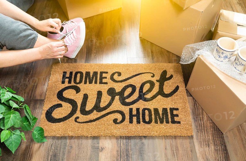 Woman wearing sweats and untying pink shoes near home sweet home welcome mat