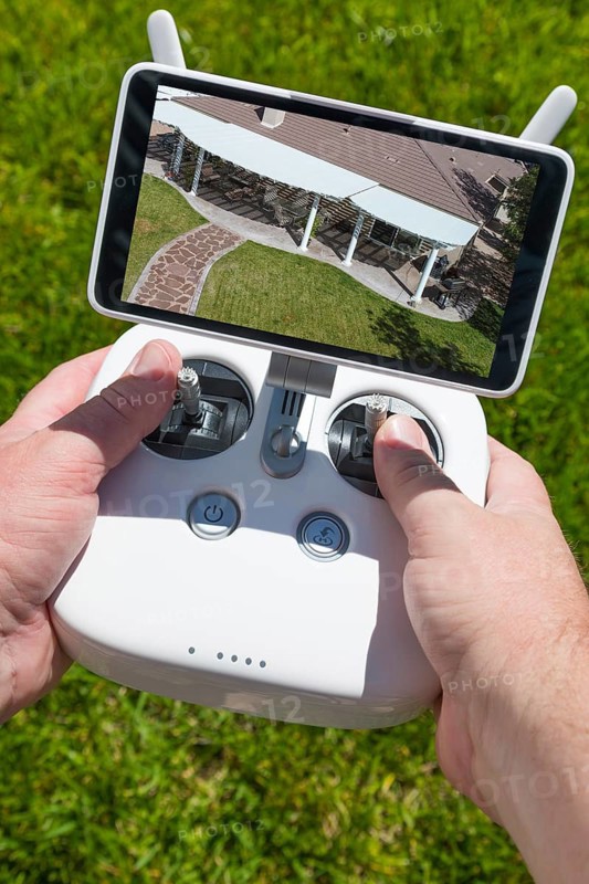 Hands holding drone quadcopter controller with overhead of house on screen