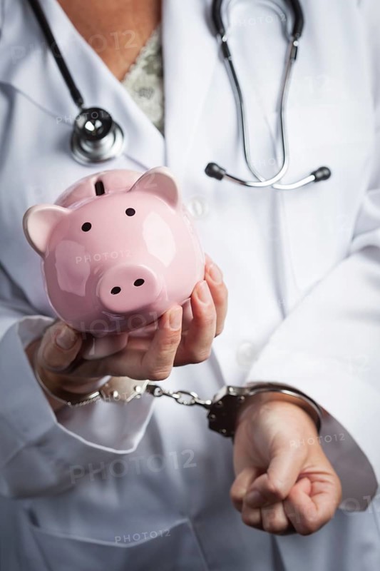 Female doctor or nurse in handcuffs holding piggy bank wearing lab coat and stethoscope