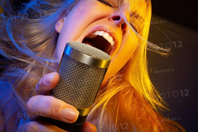 Female vocalist under gelled lighting sings with passion into condenser microphone
