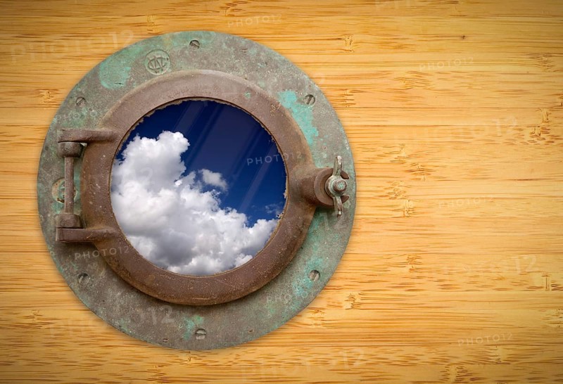 Antique porthole on bamboo wall with view of beautiful blue sky and clouds