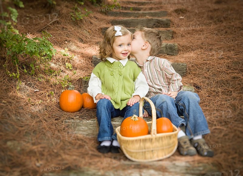 Adorable brother and sister children sitting on wood steps with pumpkins whispering secrets or kissing cheek
