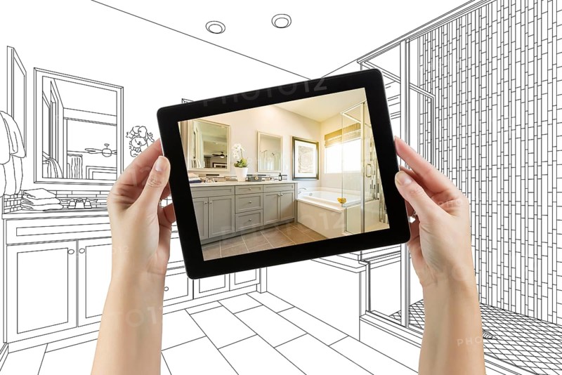Hands holding computer tablet with master bathroom photo on screen and drawing behind
