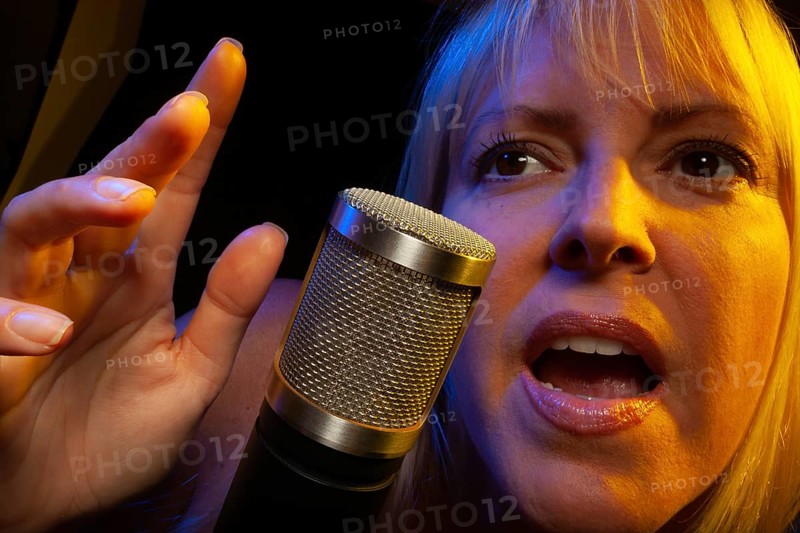 Female vocalist under gelled lighting sings with passion into condenser microphone