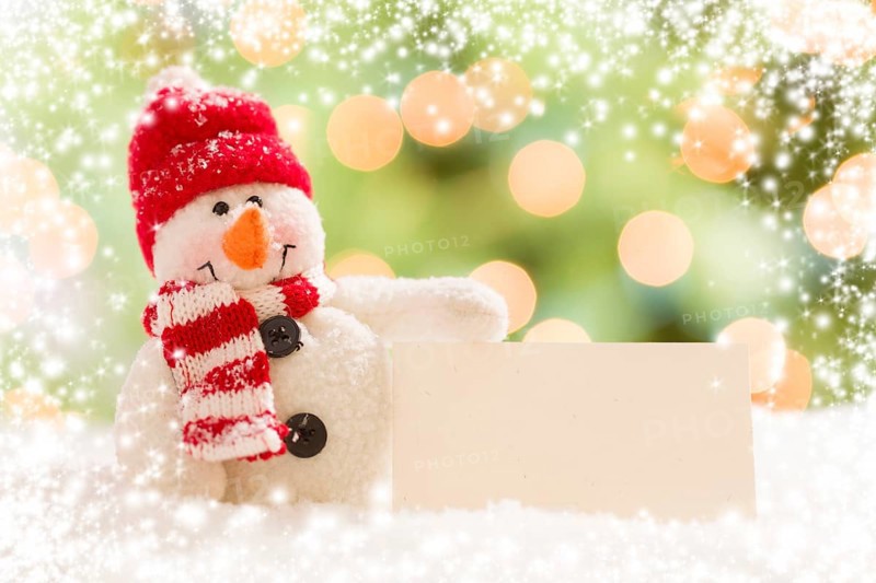 Cute snowman with scarf and hat next to blank white card over abstract snow and light background