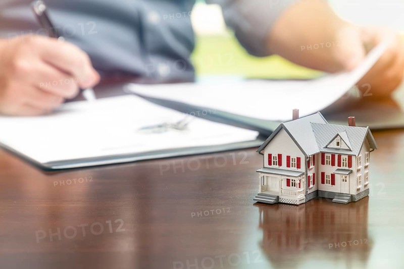 Man signing real estate contract papers with small model home in front
