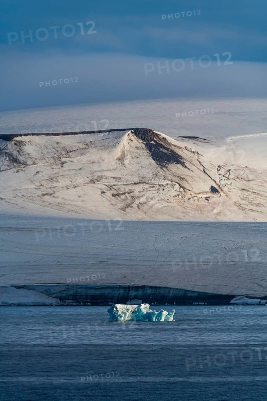 Iceberg floating before the flat table mountains covered with ice