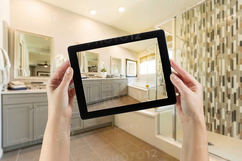 Master bathroom interior and hands holding computer tablet with photo on screen