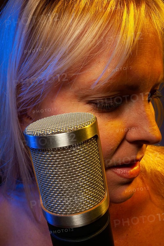 Female vocalist under gelled lighting sings with passion into condenser microphone