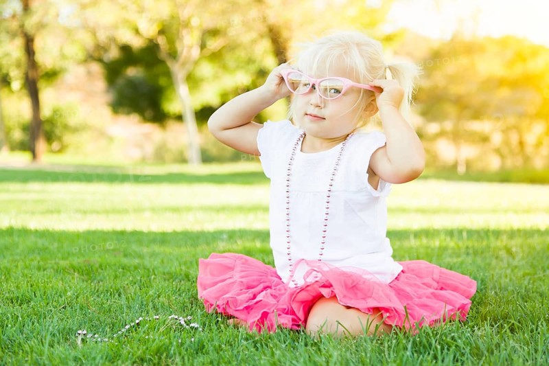 Cute little girl playing dress in the grass up with pink glasses and beaded necklace