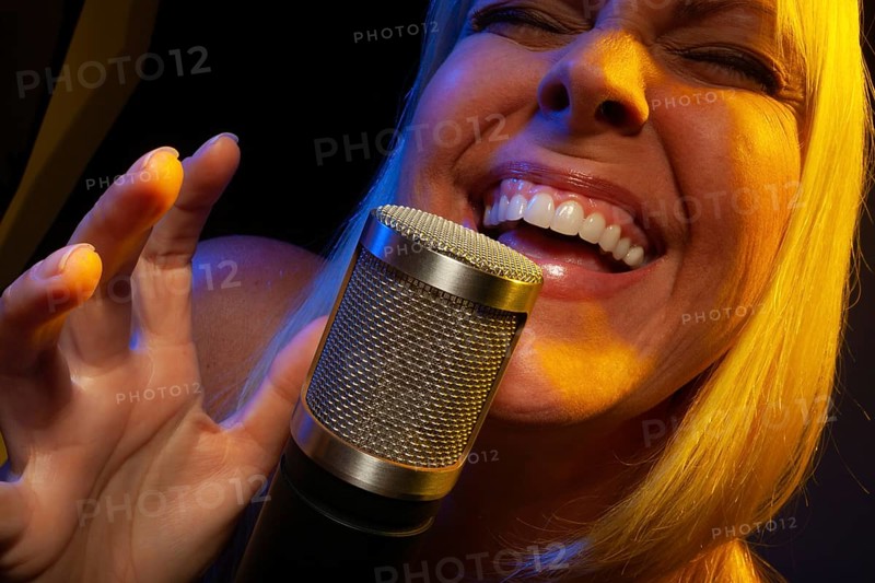 Female vocalist under gelled lighting sings with passion into condenser microphone