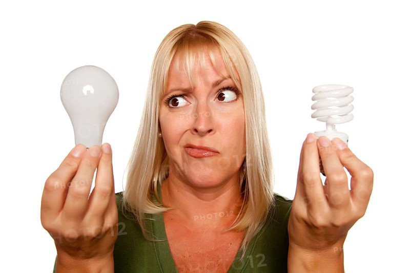 Funny faced woman holds energy saving and regular light bulbs isolated on a white background