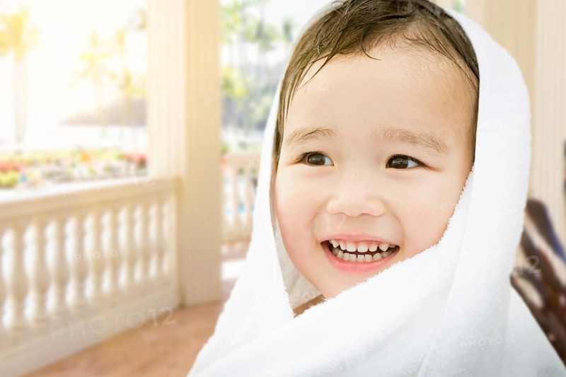 Happy cute mixed-race chinese and caucasian boy on tropical patio wrapped in A towel