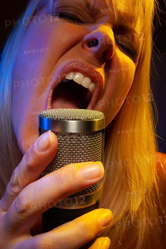 Female vocalist under gelled lighting sings with passion into condenser microphone