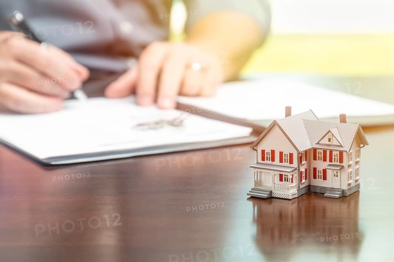 Man signing real estate contract papers with small model home in front