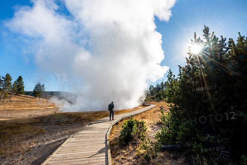 Hiker on footbridge next to steaming hot spring