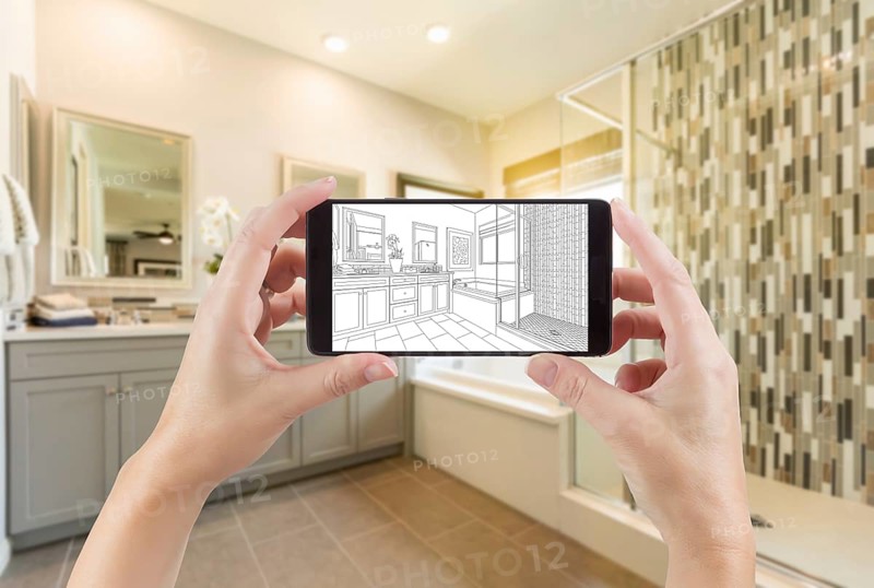 Hands holding smart phone with master bathroom drawing on screen and photo behind
