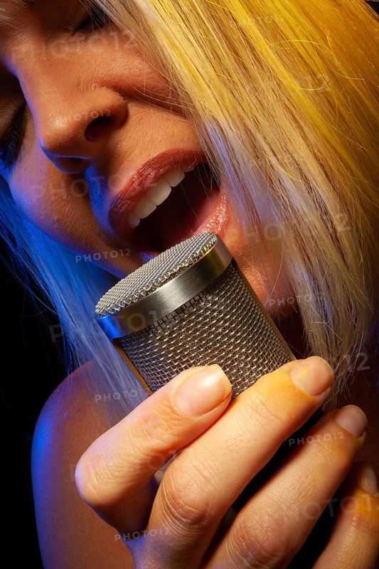 Female vocalist under gelled lighting sings with passion into condenser microphone