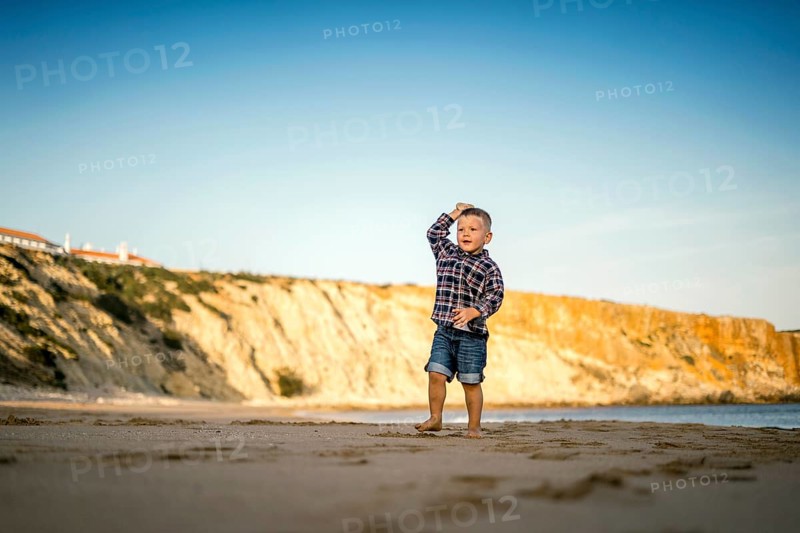 Small boy throwing stones on the beach by the sunset