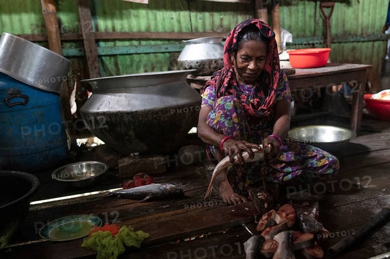 A woman sits on the floor of a cookshop scaling a fish