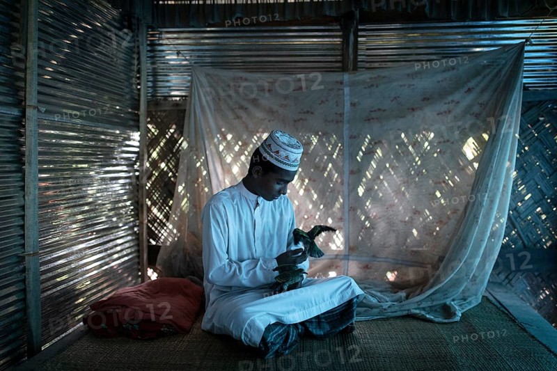 Ahmed on a raffia rug on the floor of a hut playing with two birds