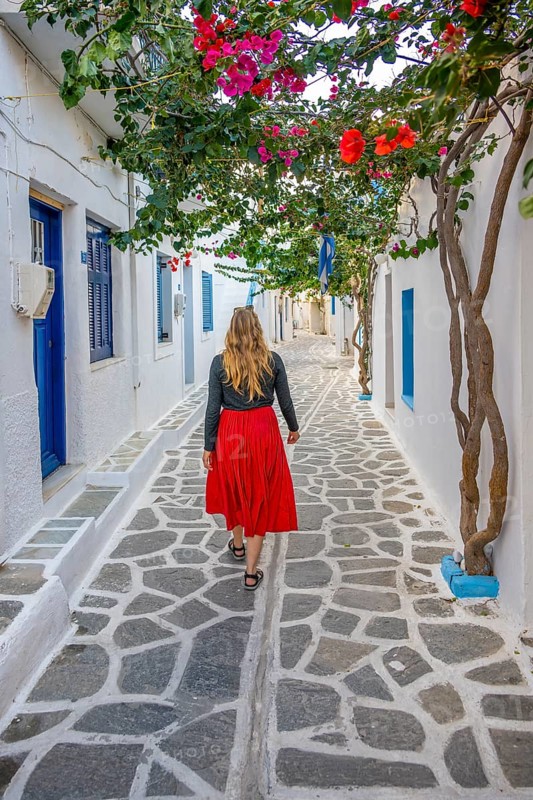 Young woman with dress walking through alley with Cycladic houses