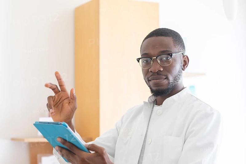 Young black doctor with smock and tablet explaining in the surgery