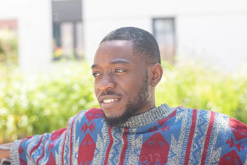 Young black man sitting on bench with African poncho