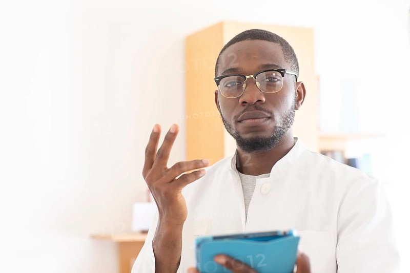Young black doctor with smock and tablet explaining in the surgery