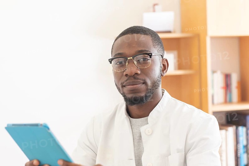 Young black doctor with smock and tablet explaining in the surgery