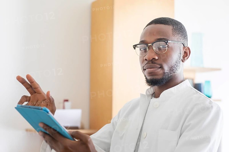 Young black doctor with smock and tablet explaining in the surgery