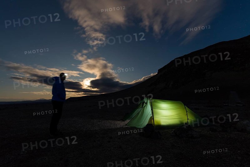 Man with headlamp standing in front of tent lit from inside
