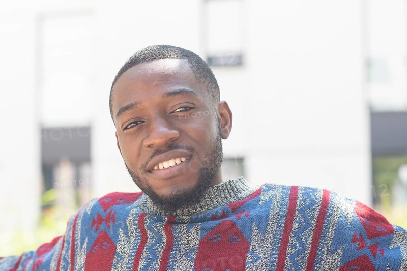 Young black man sitting on bench with African poncho