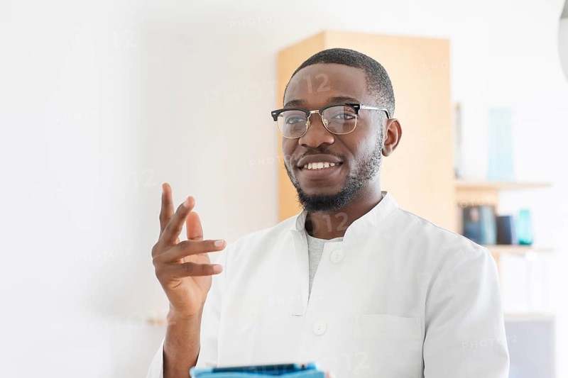 Young black doctor with smock and tablet explaining in the surgery