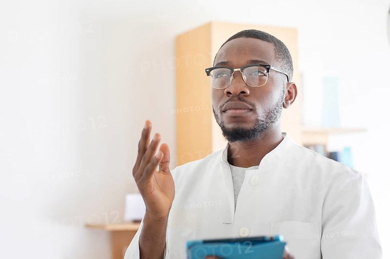 Young black doctor with smock and tablet explaining in the surgery